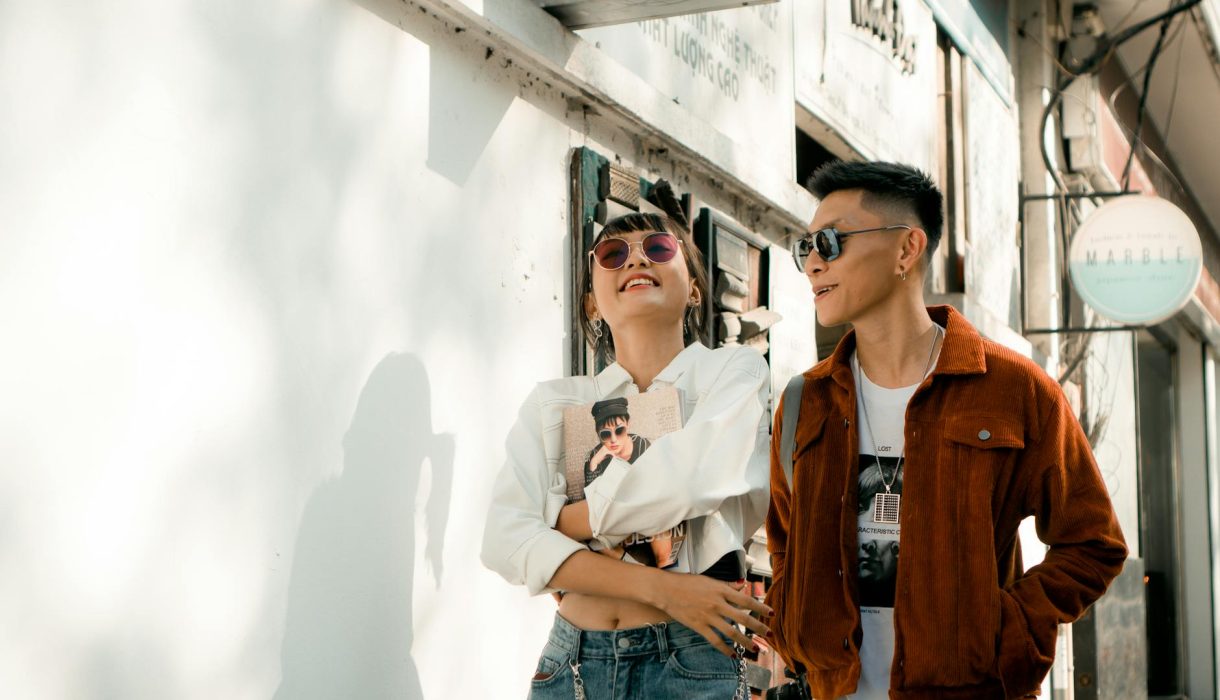 A fashion-forward couple enjoys a sunny walk in stylish outfits, exuding happiness and urban flair.